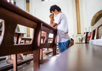 a man kneels at a pew, praying